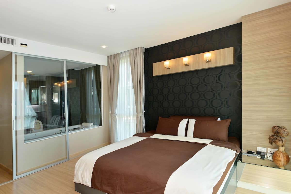 A modern hotel room with a large bed, a glass partition, and a wall-mounted light fixture.