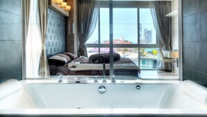 A modern bathroom with a large bathtub, a bed with pillows, and a view of a cityscape through large windows.