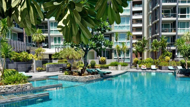 A modern hotel with a large pool area, surrounded by lush greenery and palm trees.