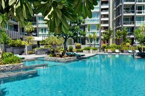 A modern hotel with a large pool area, surrounded by lush greenery and palm trees. - Luxury Style of Life (Pattaya)