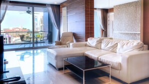 A modern living room with a white sofa, a glass coffee table, and a large window with curtains.