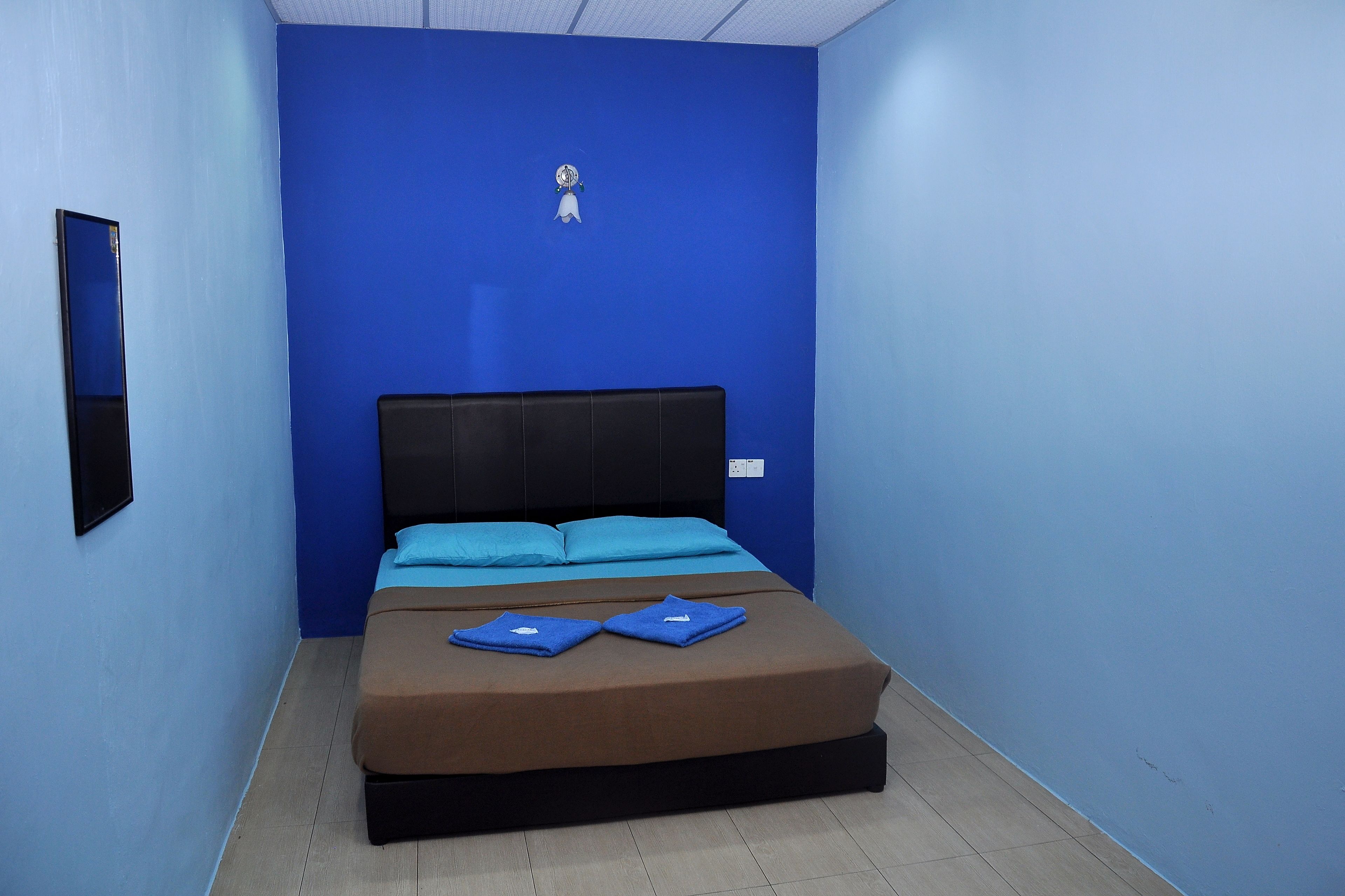 A room with a bed, blue walls, a black headboard, and a small wall-mounted light fixture.