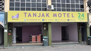 Une enseigne d’hôtel portant le nom « Tanjak Motel » et indiquant un service disponible 24 heures sur 24.