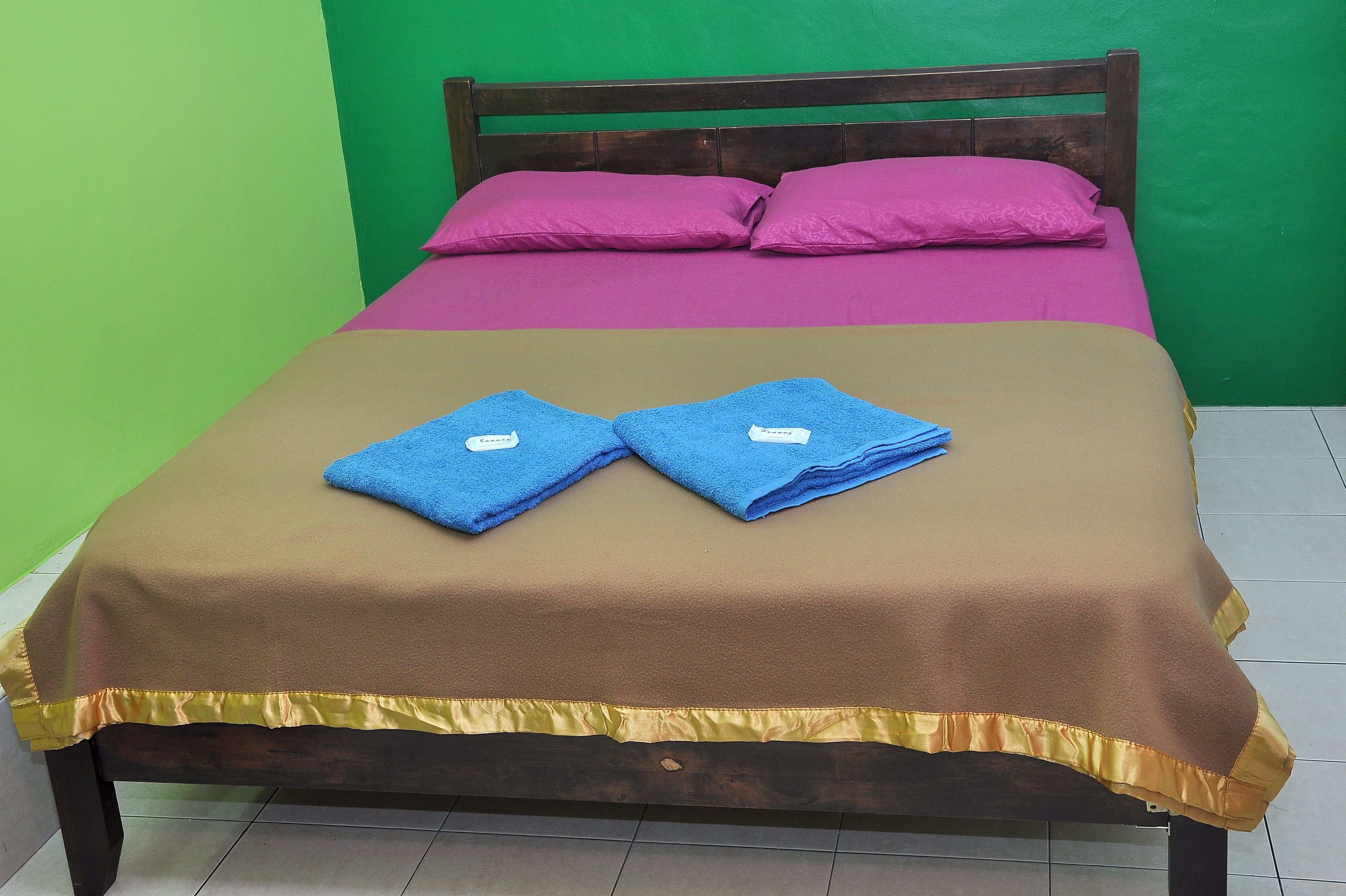 A bed with a brown and pink bedspread, two blue towels, and a wooden headboard.