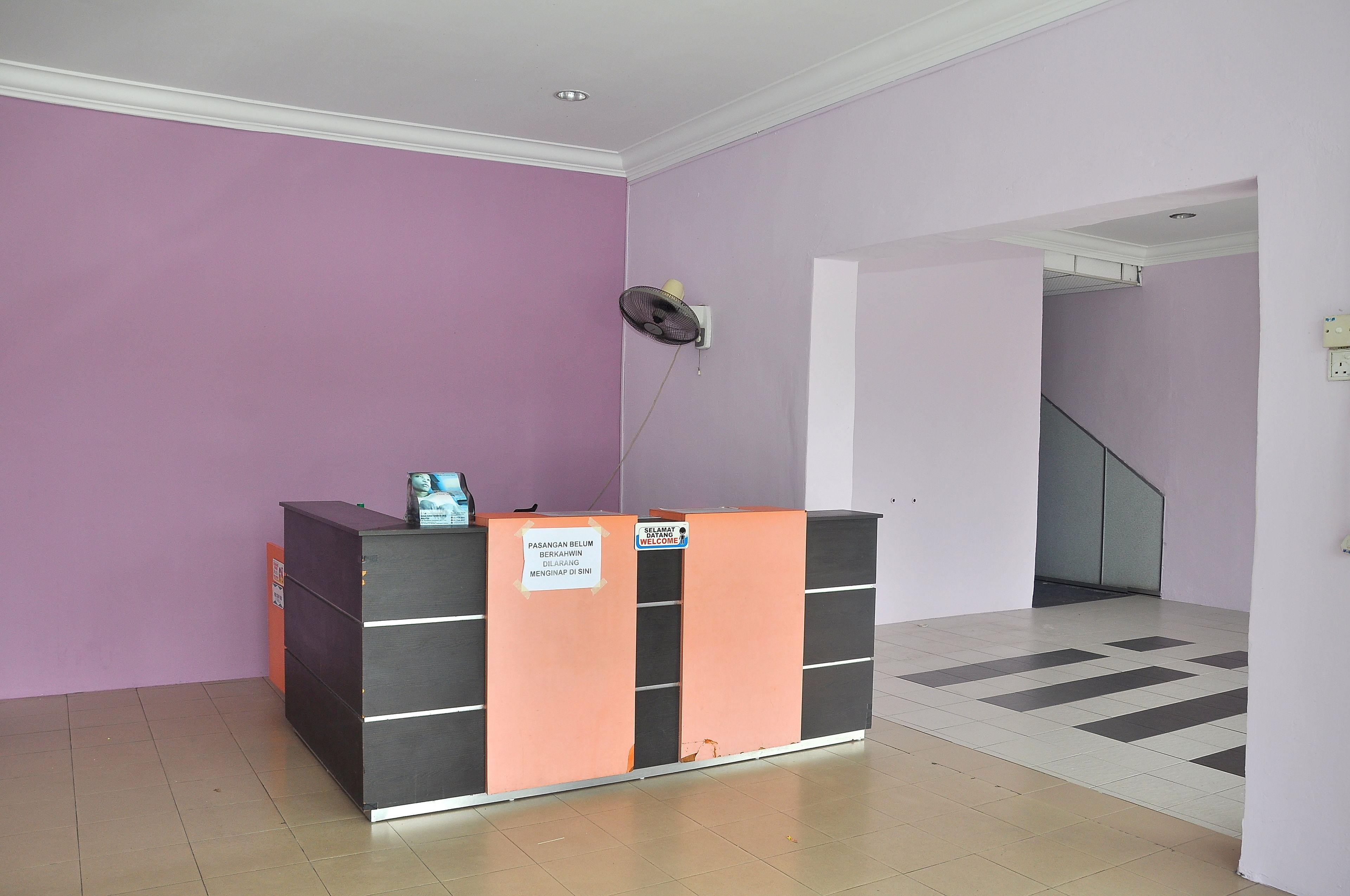A reception desk with a sign, a fan, and a staircase in the background.