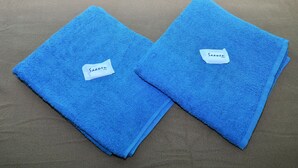 Deux serviettes bleues pliées, avec des étiquettes apposées sur une surface texturée.