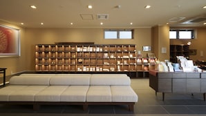 A reception area with a sofa, a display of framed items, and a counter with brochures. - WAQOO Shitaderamachi (Osaka)