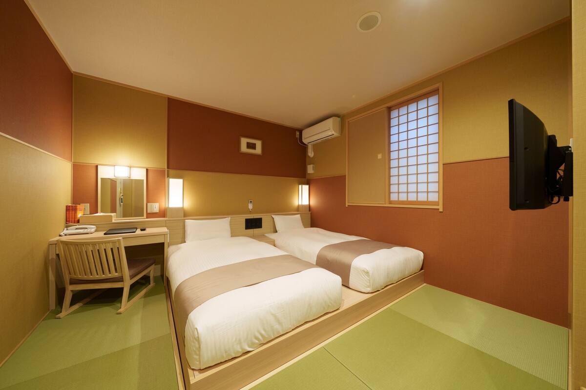 A hotel room with two beds, a desk, a chair, a TV, and a window with a view.