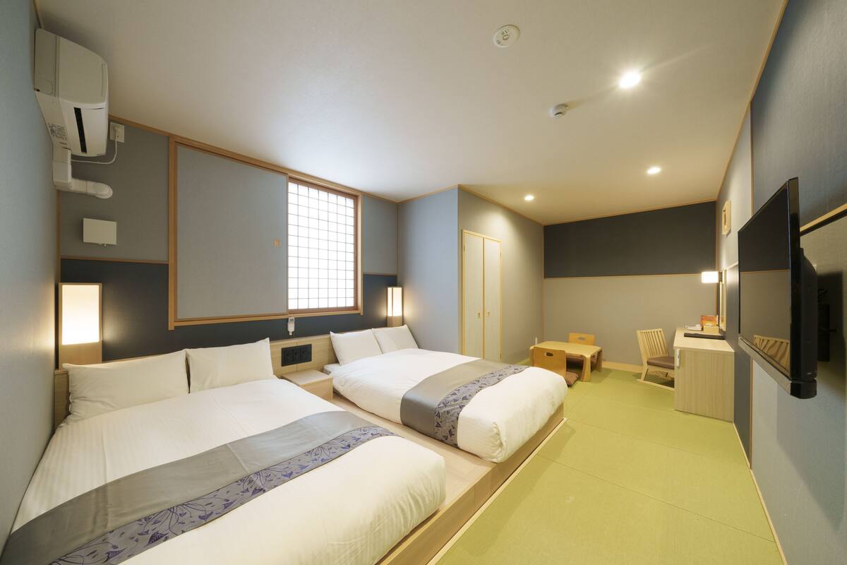 A hotel room with two beds, a desk, a chair, and a TV.