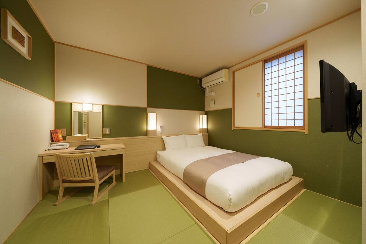 A hotel room with a bed, desk, chair, and a TV.