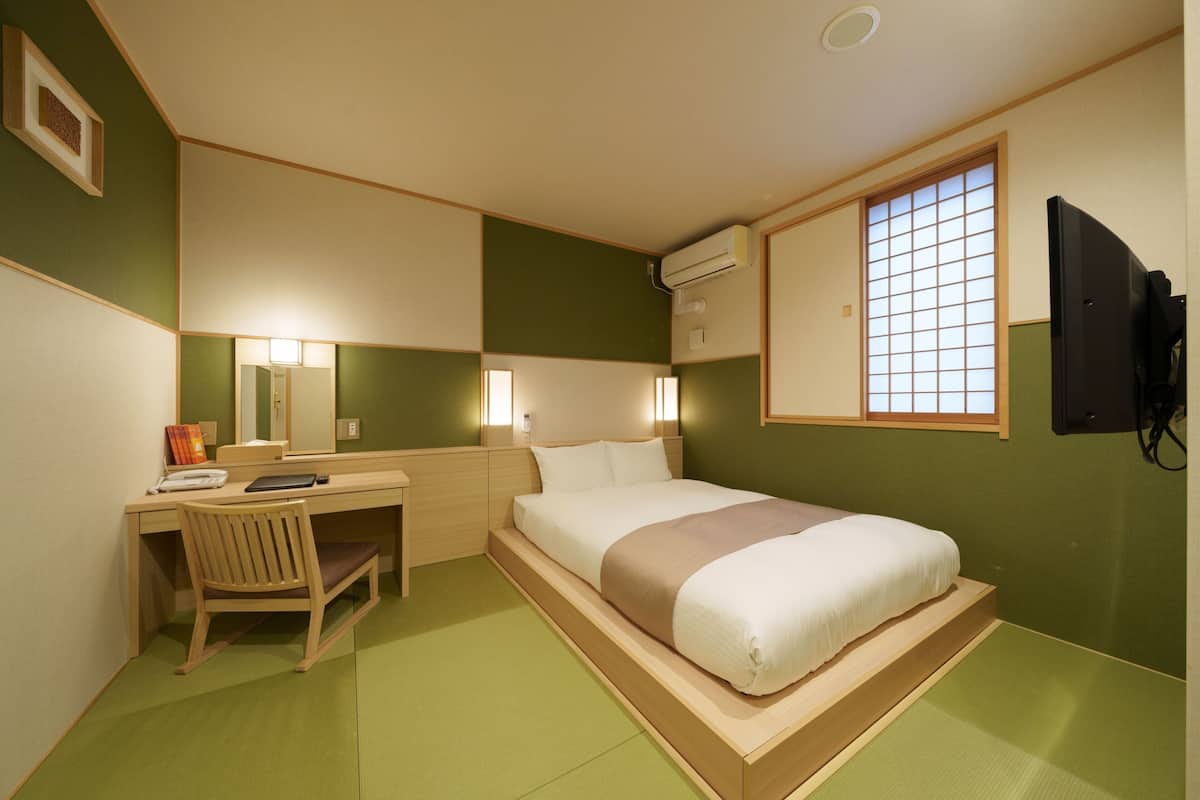 A hotel room with a bed, desk, chair, and a window with a view.