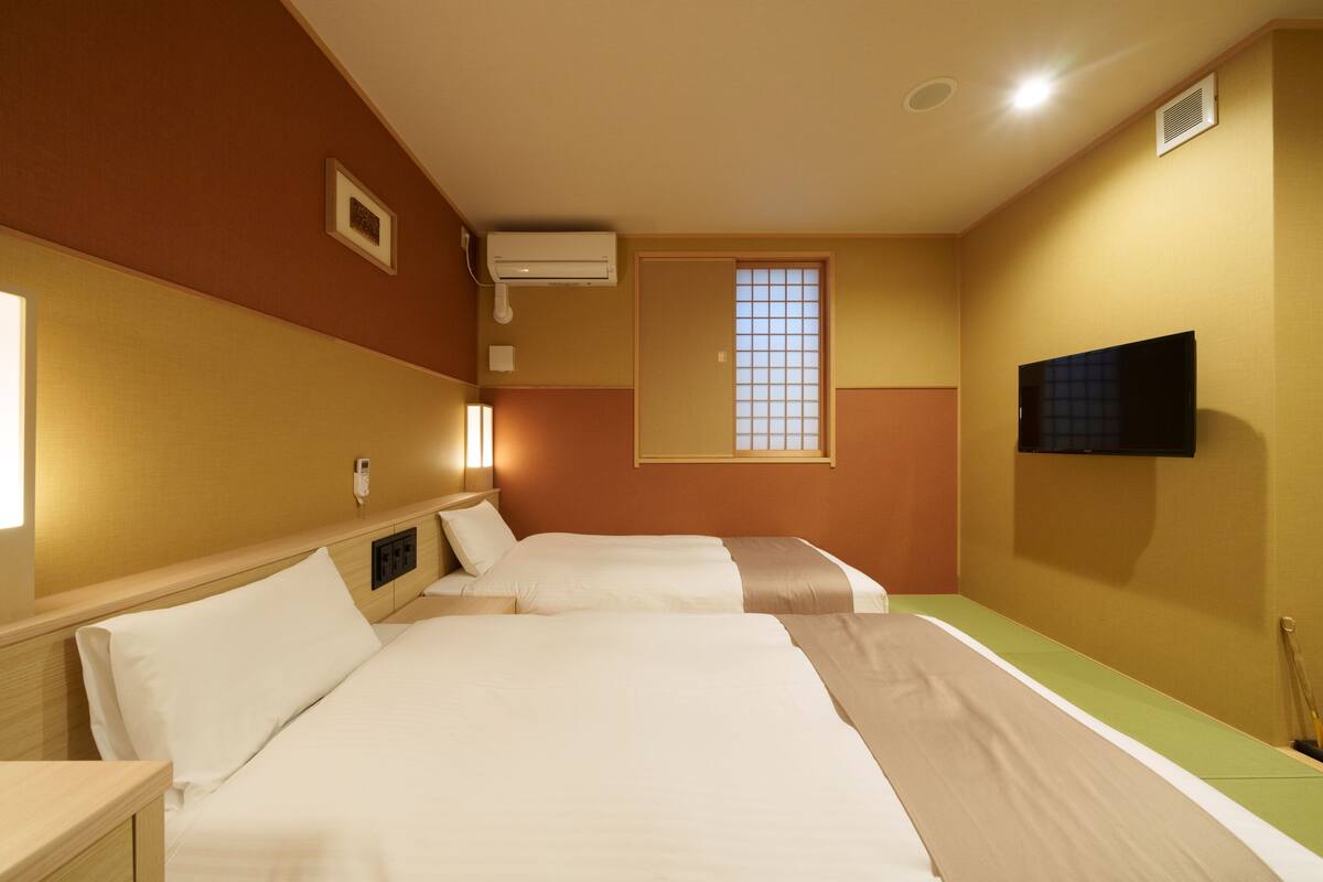 A hotel room with two beds, a television, an air conditioning unit, and a window with a view.