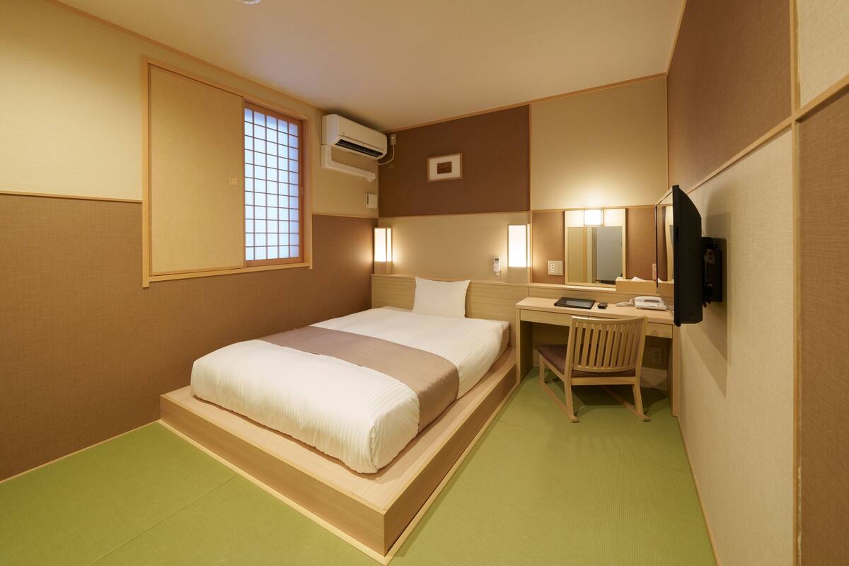 A hotel room with a bed, desk, chair, and a TV.
