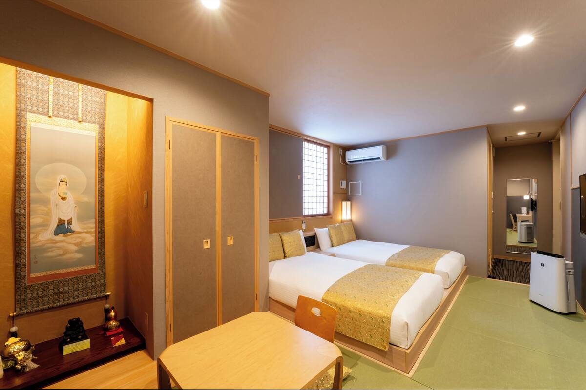 A hotel room with two beds, a desk, a chair, a TV, and a minibar.