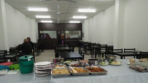 A dining area with multiple tables and chairs, a buffet table with various food items, and ceiling fans. - Diyana Budget Hotel - Hostel (Kota Bharu)
