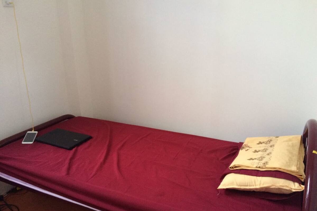 Una cama individual con un colchón rojo, un libro negro y un teléfono inteligente encima.