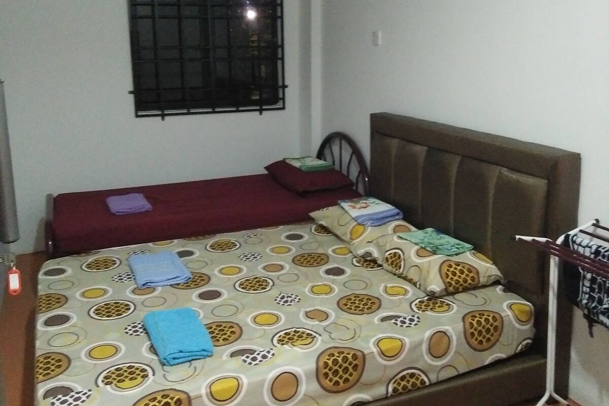 Un dormitorio con cama, una ventana con barrotes, ventilador de techo y un tendedero en la pared.