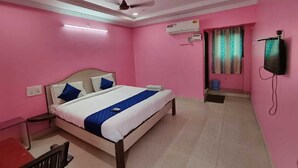Ein Schlafzimmer mit rosafarbenen Wänden, einem Bett mit weißer und blauer Bettwäsche, einem Deckenventilator, einer Klimaanlage und einem an der Wand montierten Fernseher.