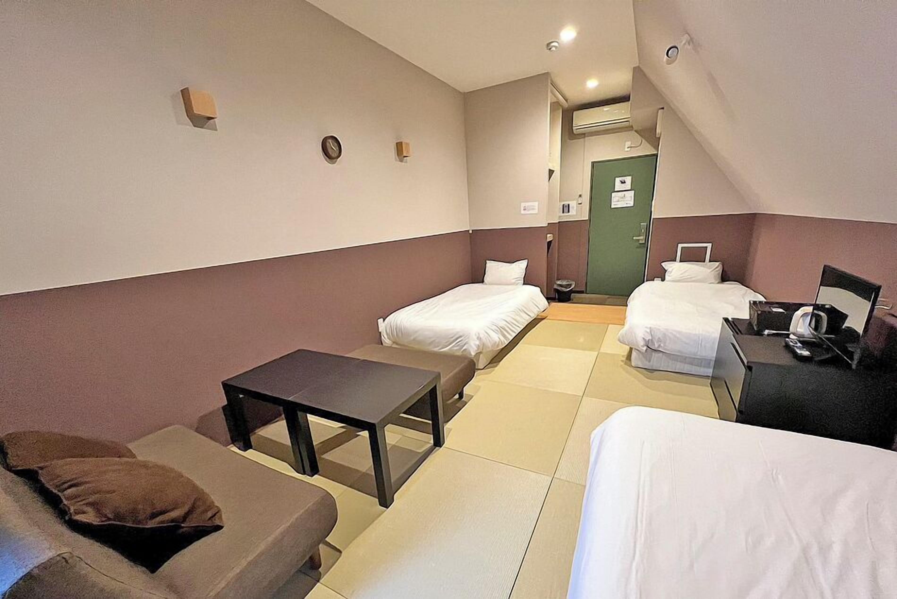 A hotel room with two beds, a small table, a sofa, and a desk with a chair.