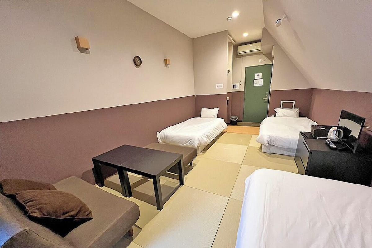 A hotel room with two beds, a small table, a sofa, and a desk with a chair.