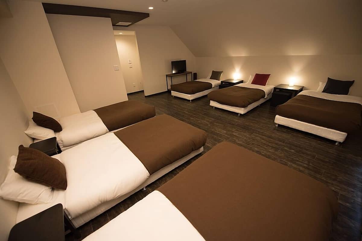 A hotel room with four beds arranged in a U-shape, a flat-screen TV, and bedside tables with lamps.