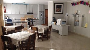 A dining area with a table set for four, a kitchen in the background, and a white desk with a computer. - Jessma Bed and Breakfast (Walvis Bay)