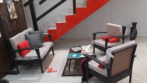 A living room with a sofa, armchair, and coffee table, a staircase with red steps, and a tiled floor. - Jessma Bed and Breakfast (Walvis Bay)