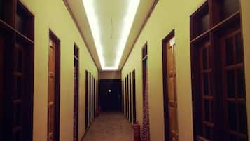 A long, narrow hallway with wooden flooring and doors on both sides, leading to a dark room at the end.