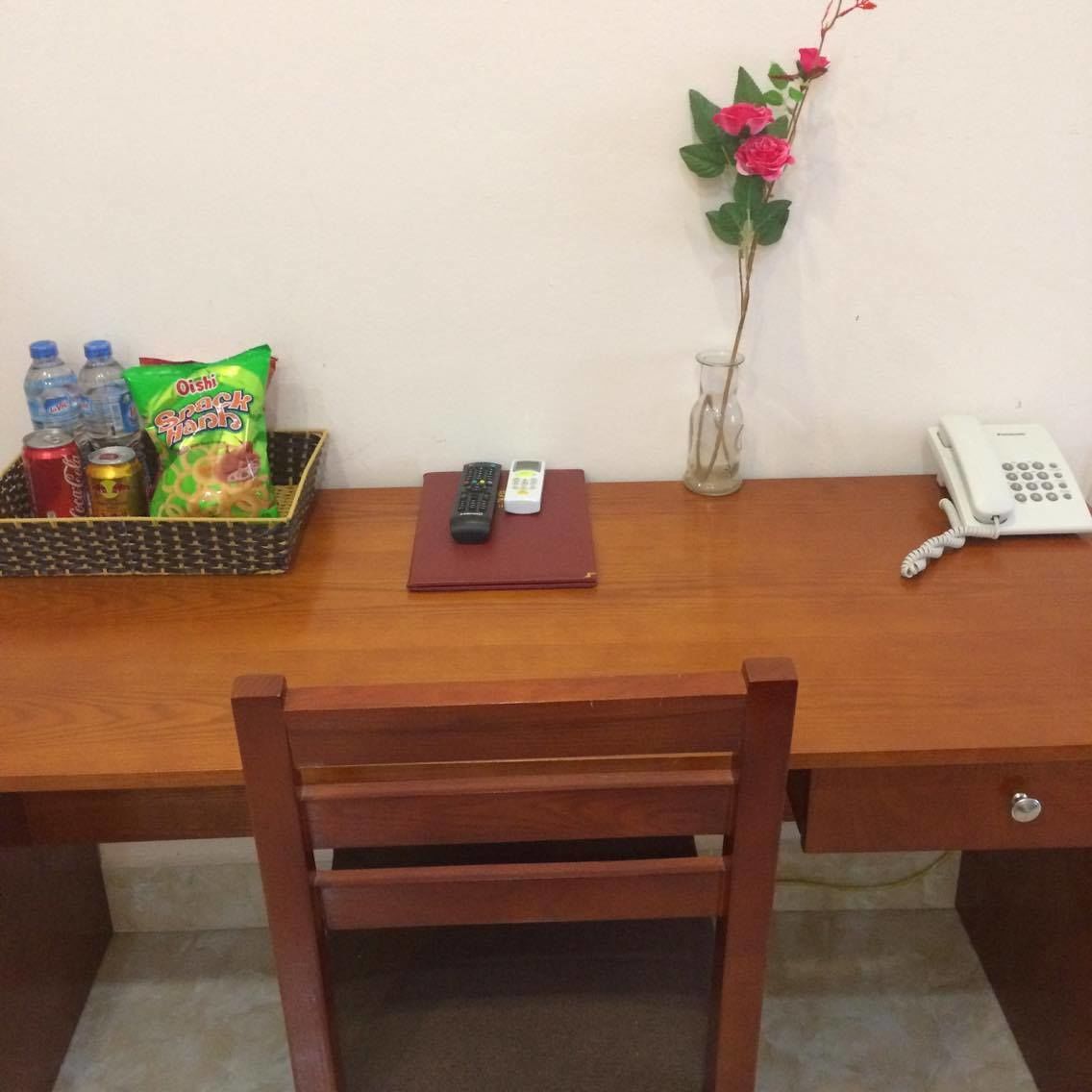 Een houten bureau met een telefoon, een afstandsbediening, een notitieboekje en lekkernijen.