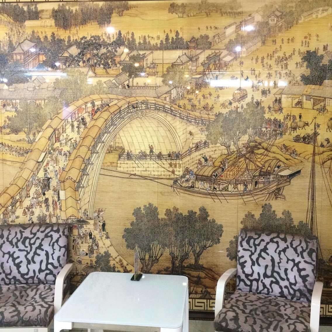 Quarto com um grande mural retratando uma cena histórica, duas cadeiras estampadas e uma pequena mesa branca.