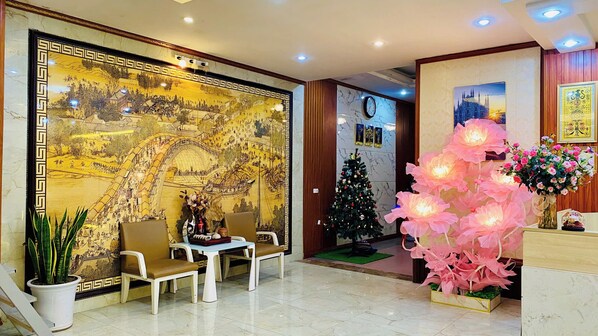 A lobby with a large mural, a Christmas tree, and a decorative pink flower arrangement. - Hoang Yen Hotel (Phan Dinh Phung)