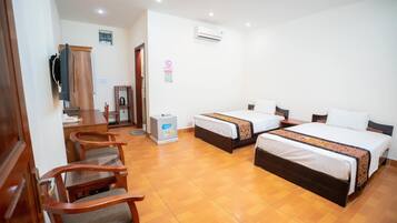 A hotel room with two beds, a desk, chairs, an air conditioner, and a refrigerator.