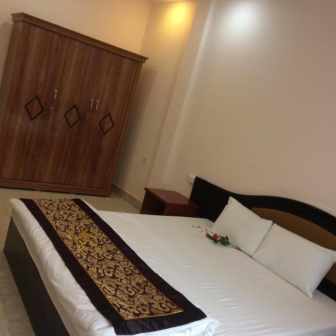 A bedroom with a large wardrobe, a neatly made bed with a decorative bedspread, and a small bedside table with a lamp.