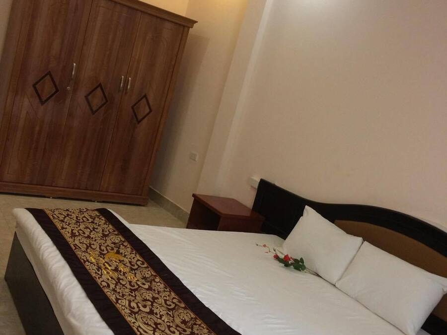 A bedroom with a large wardrobe, a neatly made bed with a decorative bedspread, and a small bedside table with a lamp.
