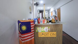 Un comptoir d’accueil avec une pancarte indiquant « SPOT ON », un ventilateur et des drapeaux de la Malaisie et des États-Unis.