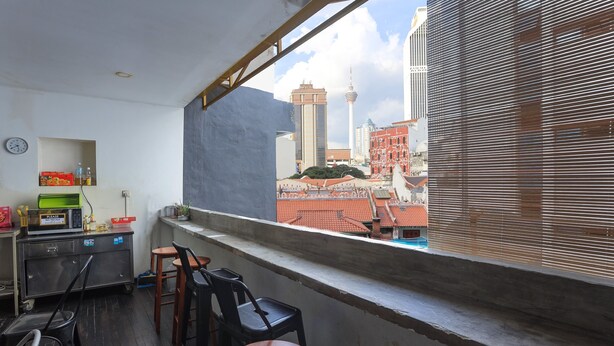 Un balcon avec vue sur le paysage urbain, comprenant une haute tour et un bâtiment avec un toit rouge. On y trouve deux chaises et une table.