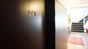 Een deur met het nummer 208, die leidt naar een trap en een kamer met een rood tapijt.