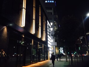 Een straatbeeld 's nachts met verlichte gebouwen en voetgangers.