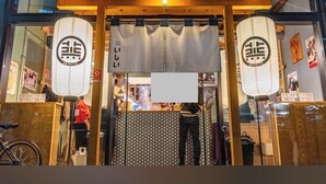 Een restaurantentree met een houten gevel, twee lantaarns en een naambord.
