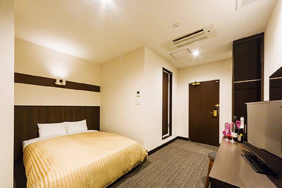 Una habitación de hotel con una cama, un escritorio, un televisor y una puerta.