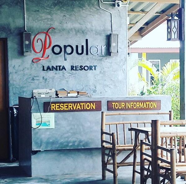 A reception desk at Lanta Resort with 'Popular' signage, 'RESERVATION' and 'TOUR INFORMATION' signs, and a wooden chair in front. - Popular Lanta Resort (Ko Lanta)