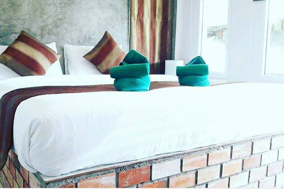 A bed with white bedding, two striped pillows, and two green folded pillows.