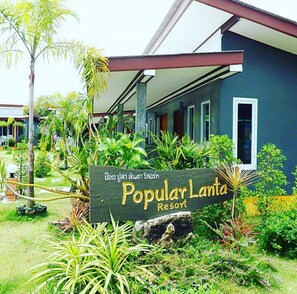A sign for Popular Lanta Resort surrounded by lush greenery and a modern building structure. - Popular Lanta Resort (Ko Lanta)