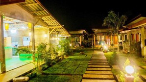Vista noturna de um resort com calçada pavimentada, área de estar ao ar livre e edifícios bem iluminados.
