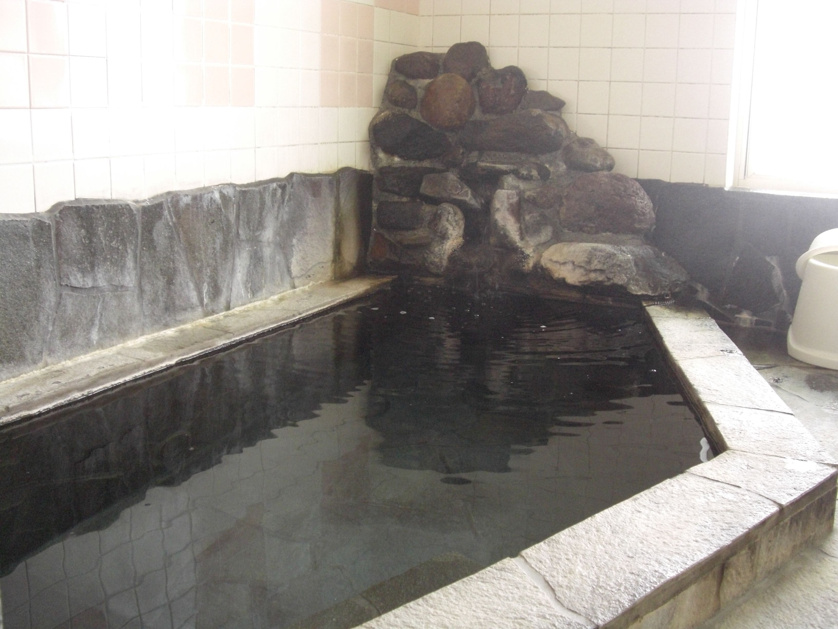 A stone-lined hot tub with a tiled wall in the background.