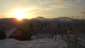A snow-covered landscape with a cabin and mountains in the background.