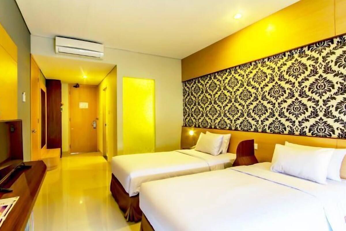 A hotel room with two beds, a desk with a computer, and a patterned headboard.
