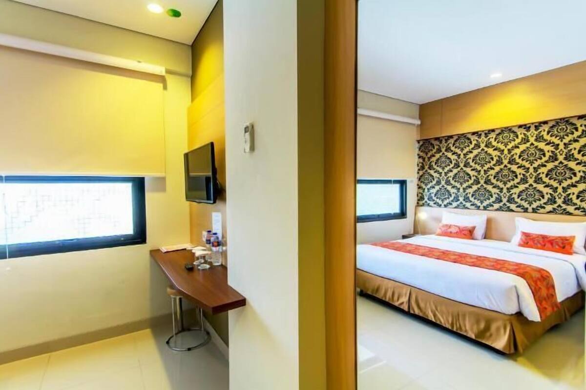 A hotel room with a bed, a desk, a television, and a window.