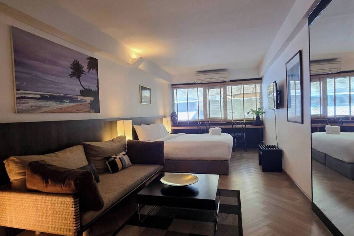 A modern hotel room with a sofa, a bed, a dining table, and large windows offering a view of the ocean.