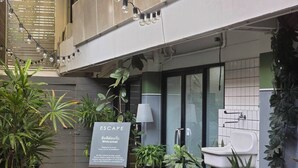 A courtyard with potted plants, a sign reading "ESCAPE Welcome! Please let us know if we can be of assistance", and a bathtub. - Somewhere to Escape - Hometel (Bangkok)
